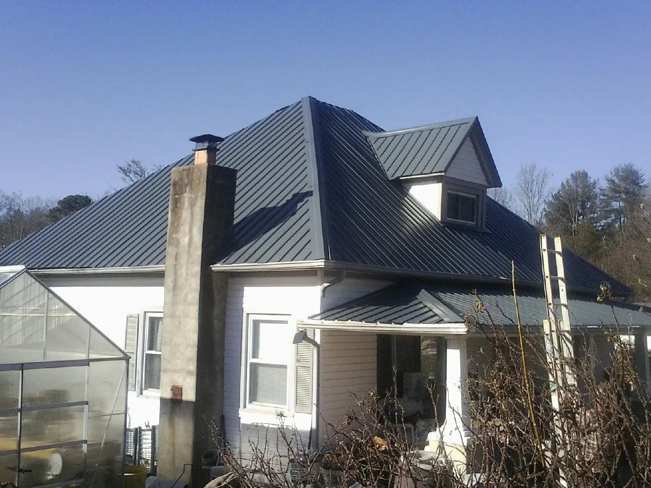 Dark blue standing seam metal roof on a white farmhouse with dormer — Slate & Tile Roof Repair by Roofing Brothers in Newsoms