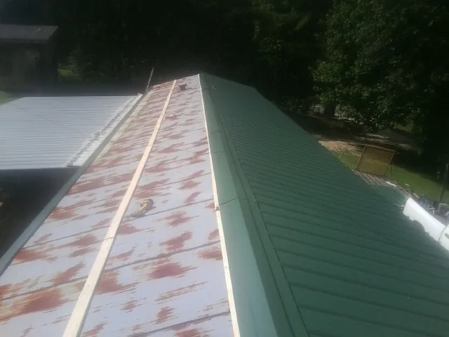 Old rusted panels beside newly installed green metal roofing — Wind Damage Roof Repair by Roofing Brothers in Newsoms