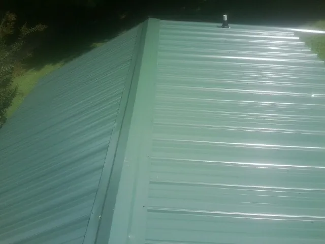 New green metal panels meeting at the ridge of a roof — Flat Roof Repair work by our crew in Newsoms