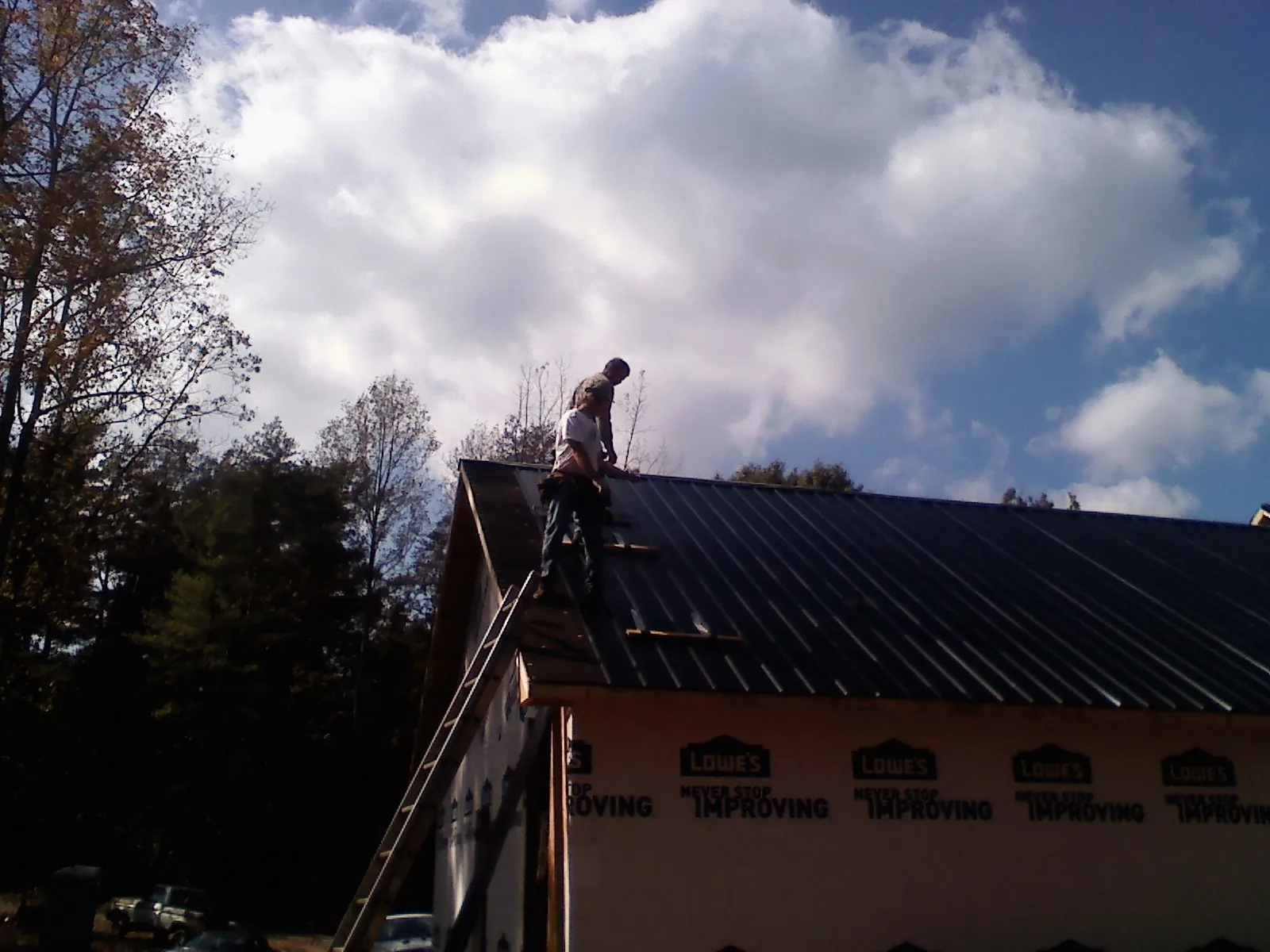 Roofer fastening dark metal panels high against a cloudy sky, from a Roof Inspection job in Newsoms