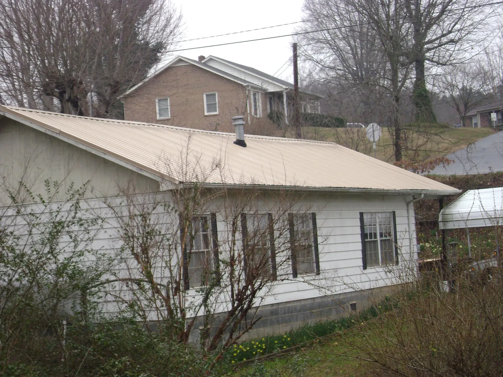 Tan metal roof on a white sided house set into a hillside — Commercial Roofing by Roofing Brothers in Newsoms