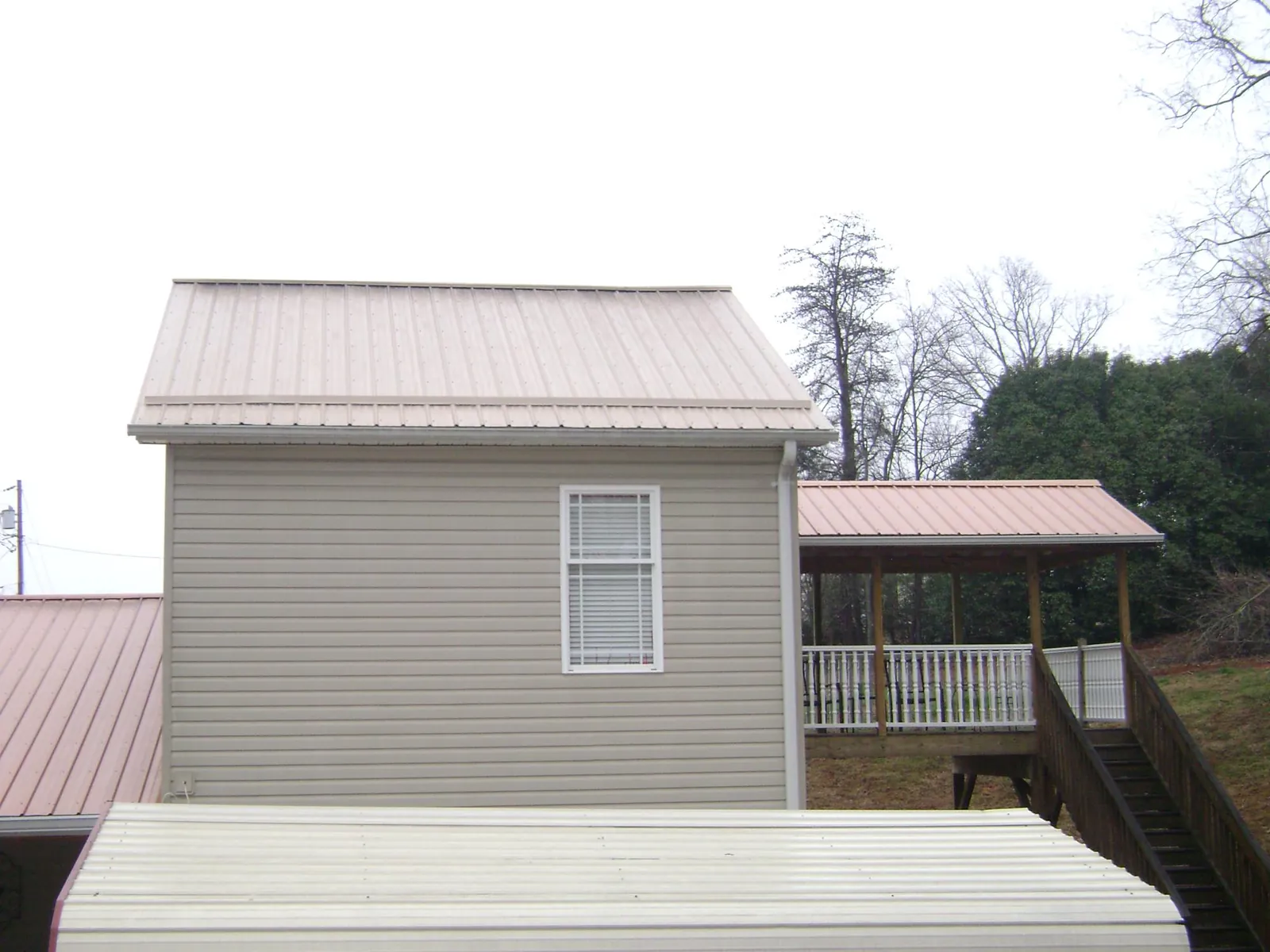 Tan metal roofs on a two story addition and attached porch, from a Roof Replacement job in Newsoms